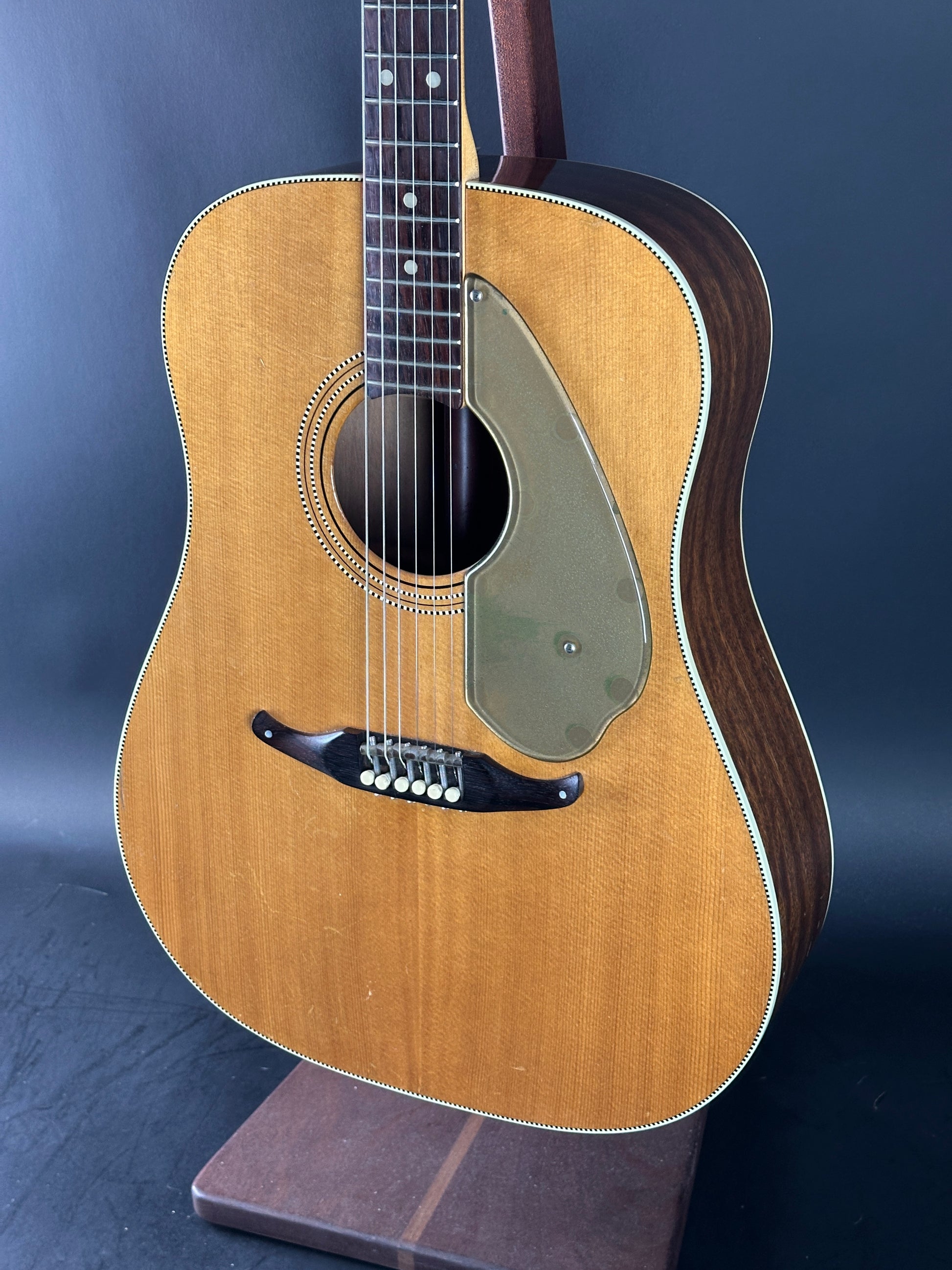 Acoustic guitar on a stand against a dark background