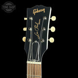 Close-up of the headstock of a Gibson Les Paul Special acoustic guitar against a solid black background, featuring gold lettering and cream tuning pegs.