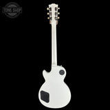 A white electric guitar shown from the back against a solid black background, featuring a white body with black pickups and a white neck with gold tuning pegs.
