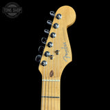 Close-up of a Fender Stratocaster electric guitar headstock made of natural maple wood, featuring six silver tuning pegs and the Fender logo, set against a solid black background.