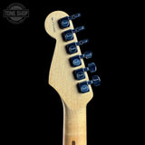 Close-up of the headstock of a Fender electric guitar in natural wood finish with blue tuning pegs, shown against a solid black background.