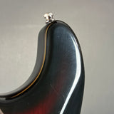 Close-up of the upper bout corner of a glossy dark electric guitar body, showing a silver tuning peg and a thin gold binding line against a neutral gray background.