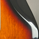 Close-up of a glossy sunburst electric guitar body showing the warm orange-brown wood grain fading into black, with a white highlight from lighting.