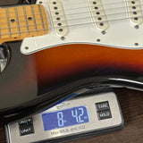 Close-up of a sunburst electric guitar body resting on a digital scale, with the scale displaying 8 lbs 4.2 oz.