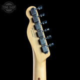 Close-up of the headstock of a Fender Stratocaster electric guitar, showing the light natural wood neck, six black tuning pegs, and 'FENDER' branding on a solid black background.