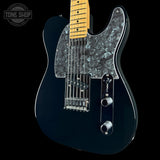 A black electric guitar with a glossy black finish, a black mother-of-pearl pickguard, and a natural maple neck, shown against a solid black background with a Tone Shop watermark in the top left corner.