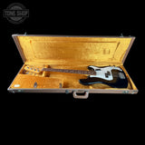 A four-string bass guitar with a black body and white pickguard resting inside an open gold-lined hard case, shown against a solid black background.