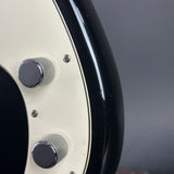 Close-up of a glossy black and cream electric guitar body with two silver control knobs and small silver screws, photographed against a dark gray background.