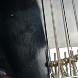 Close-up of a black bass guitar body with six strings over a chrome bridge and tailpiece.