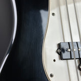 Close-up of a bass guitar body showing a glossy black top, cream pickguard, silver hardware, and part of the neck.