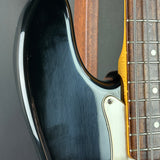Close-up of a black electric guitar body with a white pickguard and part of the brown fretboard visible.