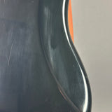 Close-up of a glossy black curved surface, likely part of a guitar body, with visible scratches and a small orange accent visible in the background.