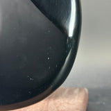 Close-up of a glossy black curved object, likely part of a guitar body, resting on a wooden surface against a neutral gray background.