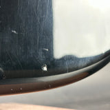 Close-up of a scratched and damaged black car window glass with visible dust, scratches, and a small chip near the edge.