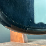 Close-up of a glossy dark blue glass bowl resting on a wooden stand, showing visible scratches and wear on the curved glass surface.