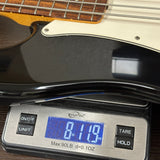 Close-up of a black electric bass guitar body resting on a digital scale displaying 8.19 lbs.