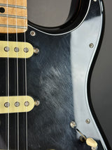 Close-up of a black electric guitar body with gold hardware, showing the pickguard, pickups, and part of the neck on a dark background.