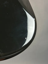 Close-up of a glossy black curved surface, likely a mirror or polished metal edge, reflecting a bright white light against a neutral gray background.