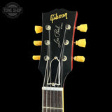Close-up of a Gibson Les Paul Model acoustic guitar headstock, featuring a black face with gold Gibson branding, white script Les Paul, and yellow tuning pegs against a black background.