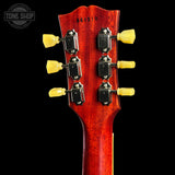 Close-up of the headstock of a six-string acoustic guitar, showing six tuning pegs with yellow grips and a glossy reddish-brown wood finish against a black background.