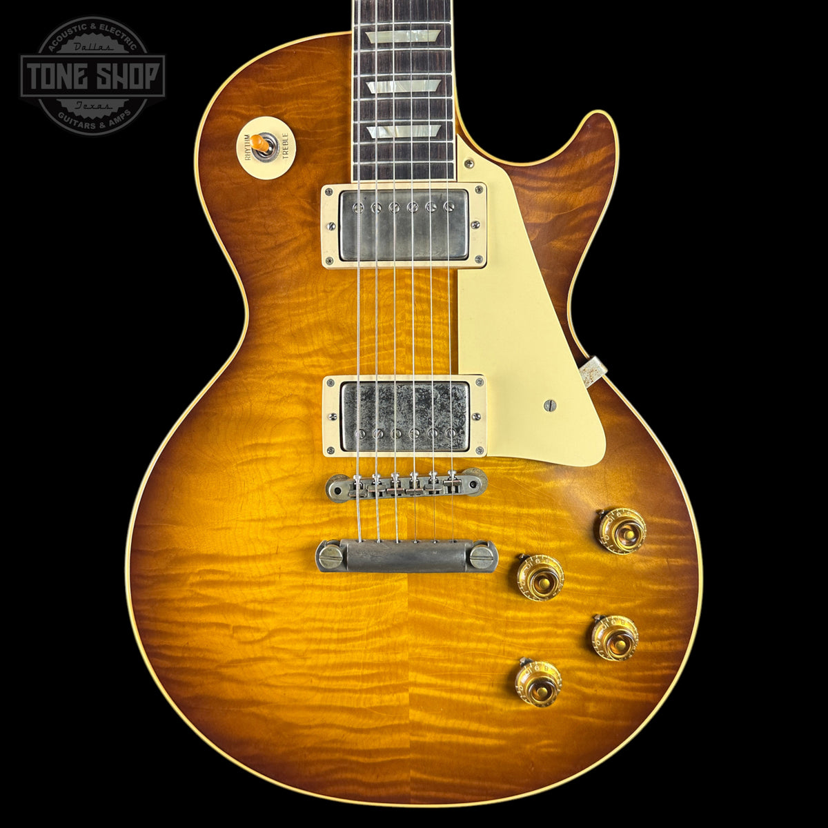 A classic electric guitar with a natural sunburst finish, featuring a cream pickguard, dual humbucker pickups, and gold-toned hardware, shown against a solid black background.
