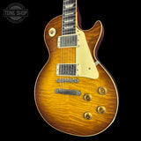 A classic electric guitar with a natural flame maple top, showing a warm golden-brown sunburst finish. It features a cream-colored pickguard, dual humbucker pickups, and gold-toned control knobs, photographed against a solid black background with a Tone Shop watermark in the upper left corner.