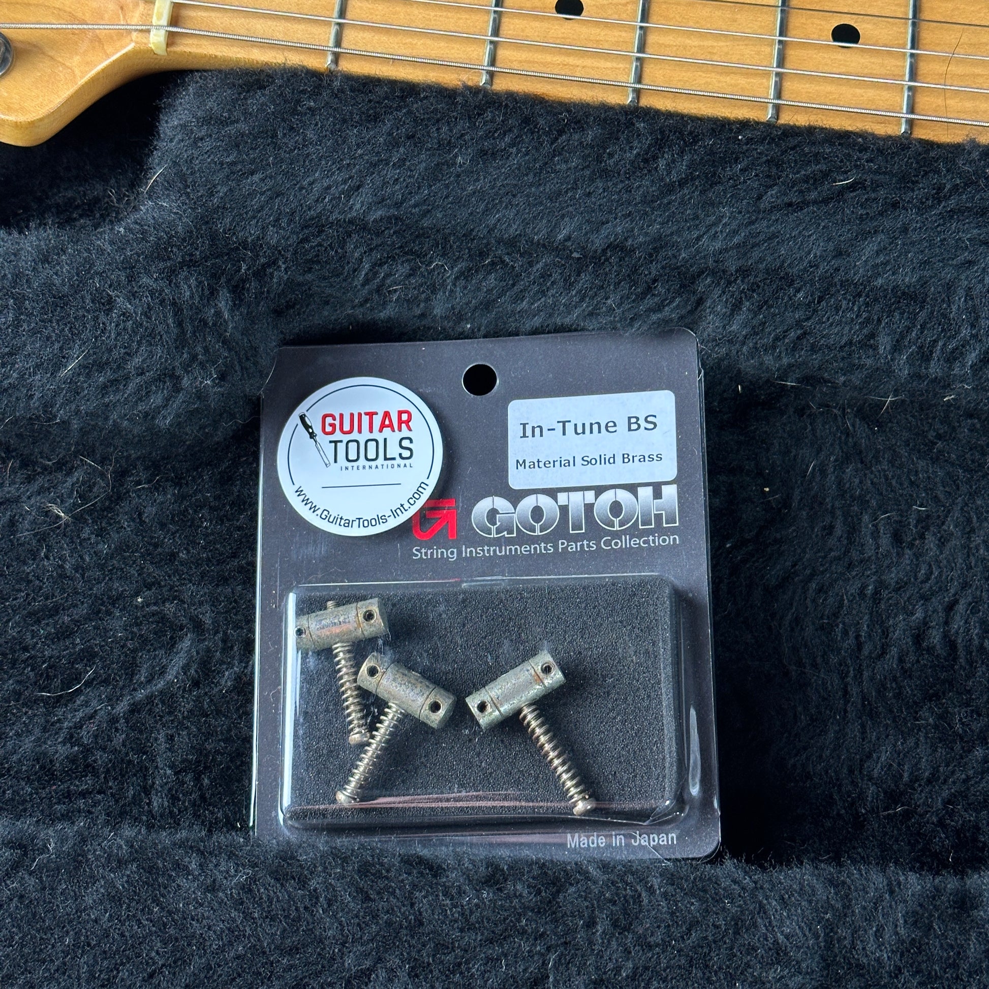 Packaged guitar parts on a black textured surface with a guitar in the background