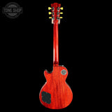 A red electric guitar shown from the back against a solid black background, featuring a glossy reddish-brown wood finish, a black pickguard, and gold tuning pegs.