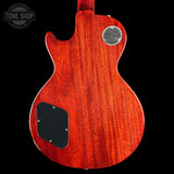 The back of a Gibson Les Paul Custom electric guitar with a vibrant reddish-orange cherry wood finish, featuring a chrome 'Gibson Les Paul Custom' badge and a black pickguard, shown against a solid black background.