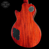 The back of a Gibson electric guitar with a glossy red-orange wood finish, featuring a black pickguard and a silver metal backplate, shown against a solid black background.