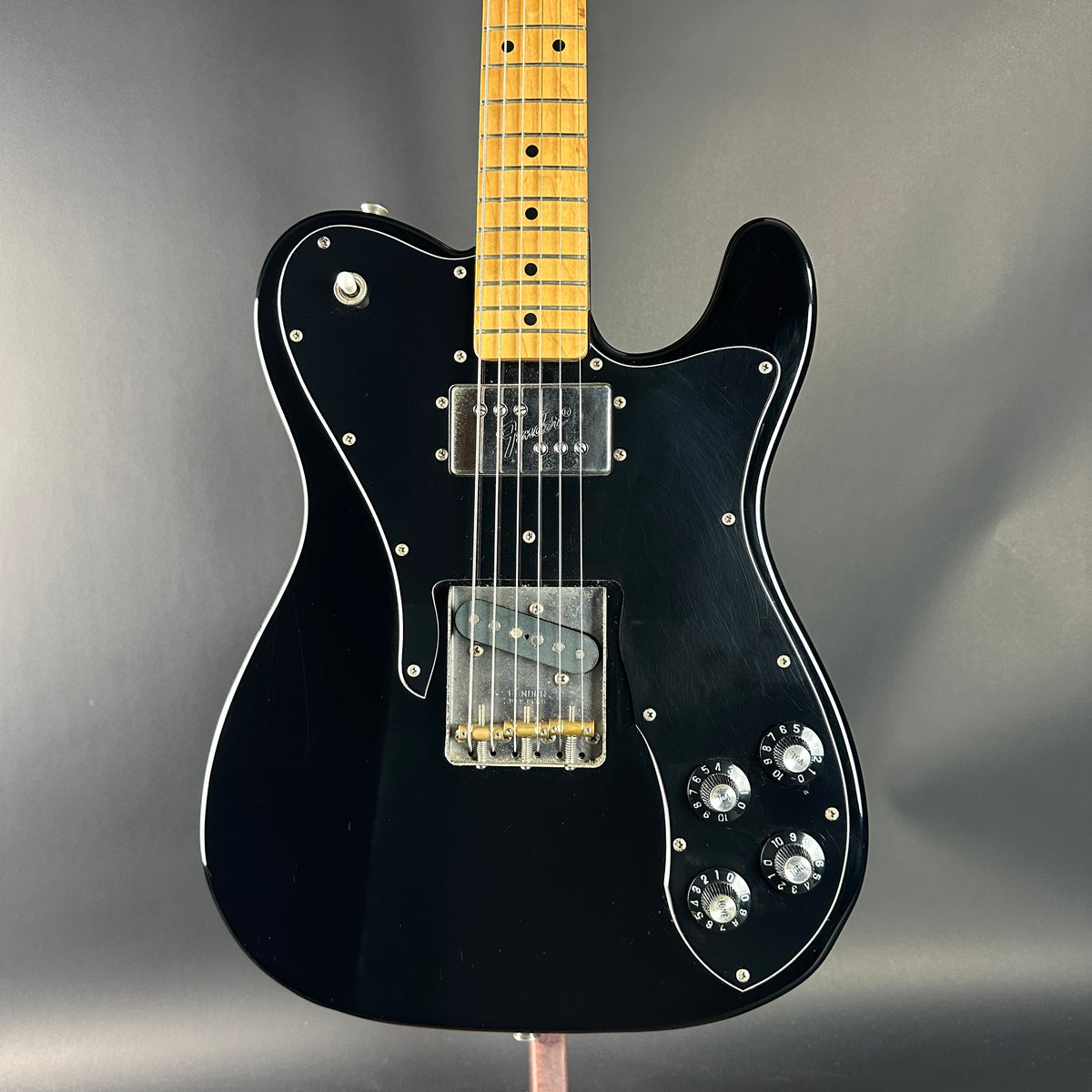 Black electric guitar with a wooden fretboard on a gray background