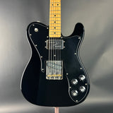Black electric guitar with a wooden fretboard on a gray background