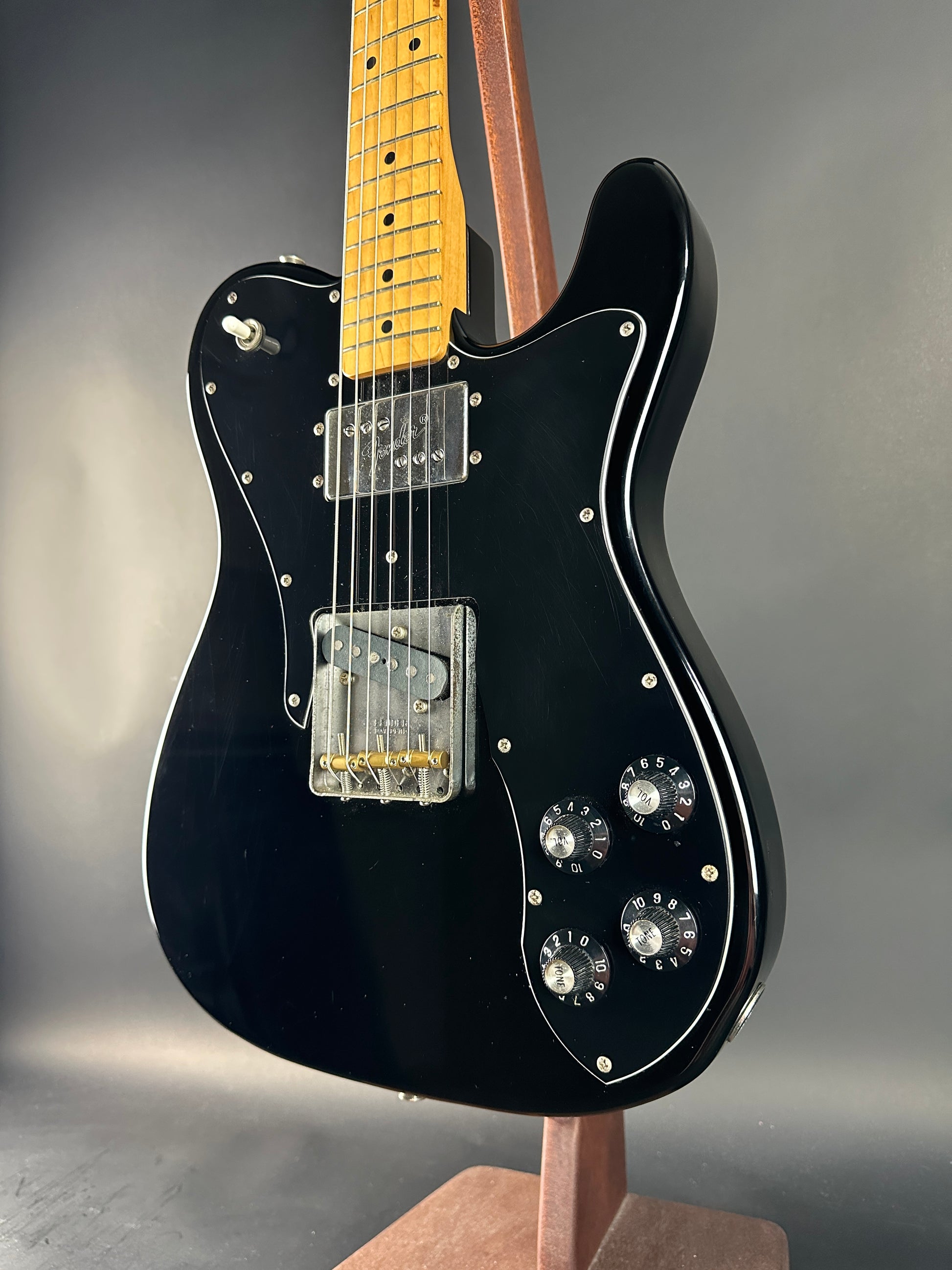 Black electric guitar with a wooden neck on a gray background