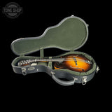 A mandolin resting inside an open hard guitar case on a black background, with a Tone Shop watermark in the top-left corner.