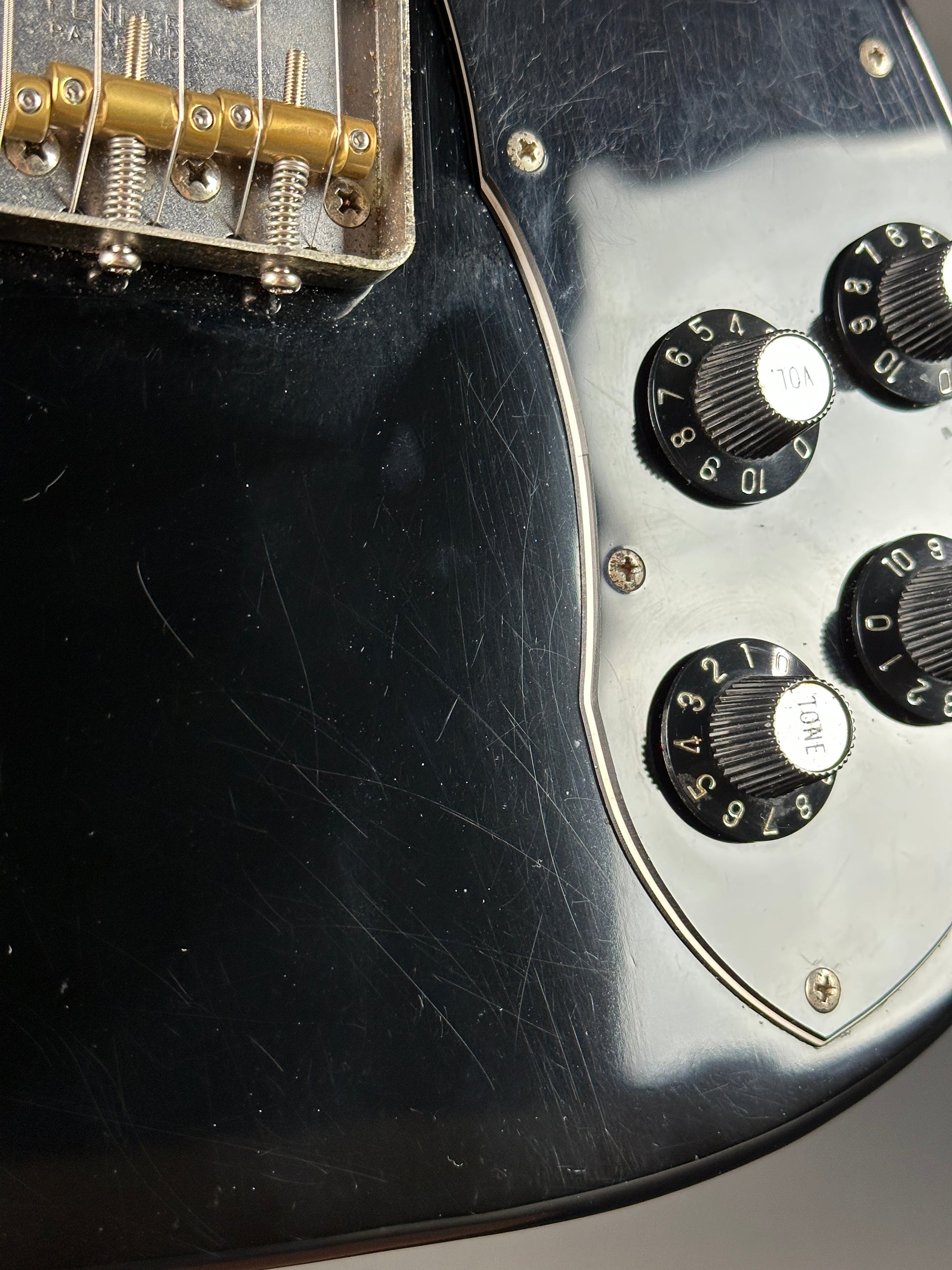 Close-up of a black electric guitar with control knobs and tuning pegs.