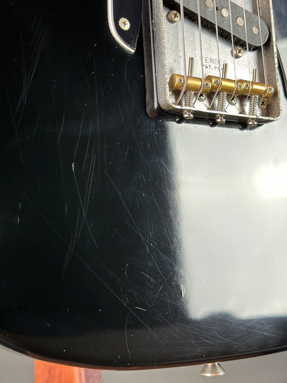 Close-up of a black electric guitar with visible wear and tear on the body.
