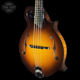A mandolin with a classic sunburst finish, transitioning from a bright amber center to a dark black outer edge, shown against a solid black background. A Tone Shop watermark is visible in the top left corner.