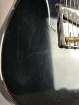 Close-up of a black electric guitar with visible wear and tear on the body.