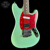Electric guitar with green body and red pickguard on a black background, featuring 'Tone Shop' logo.