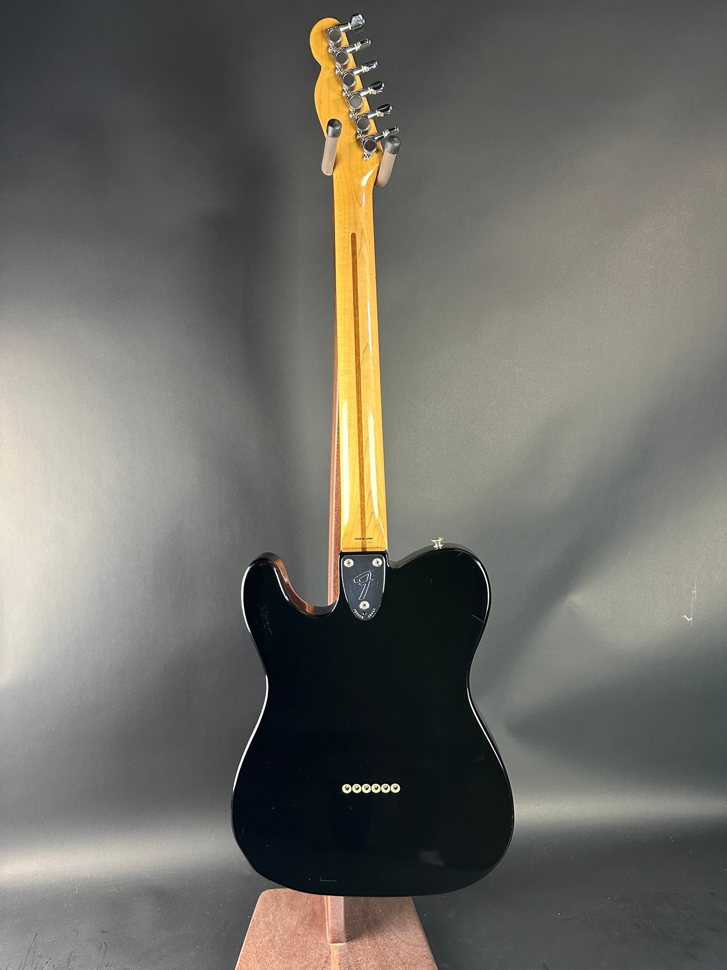 Black electric guitar with a wooden neck on a gray background