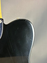 Close-up of a black guitar body with visible wear on a gray background