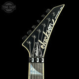 Close-up of the headstock of a Jackson electric guitar on a solid black background, showing the brand name 'Jackson' in white script and the model 'ECLECTIC 100'.
