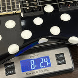 Close-up of a black electric guitar with large white polka dots resting on a digital scale displaying 8.24 lbs.