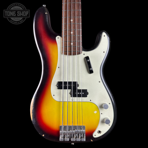 A classic bass guitar with a sunburst finish transitioning from black to orange and yellow, featuring a white pickguard and chrome hardware, shown against a black background with a Tone Shop watermark.