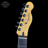 Close-up of a Fender Telecaster electric guitar headstock in natural maple wood with black tuning pegs and strings, shown against a solid black background with a Tone Shop watermark in the top left.