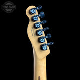 Close-up of the headstock of a guitar with a natural wood finish and blue tuners, shown against a solid black background with a Tone Shop watermark in the top left corner.