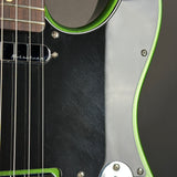 Close-up of a guitar body showing a black pickguard, silver hardware, and a bright green edge trim.