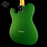 The back view of a green electric guitar against a solid black background, featuring a metallic green body, maple neck, and chrome hardware.