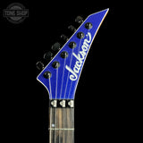 Close-up of a blue Jackson electric guitar headstock with white script logo and six black tuning pegs, shown against a black background with a Tone Shop watermark in the upper left.