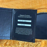 A black Gibson Custom Certificate of Authenticity booklet lies open on a yellow faux-fur surface. The insert card is printed with white text and has two light blue label areas showing serial numbers.